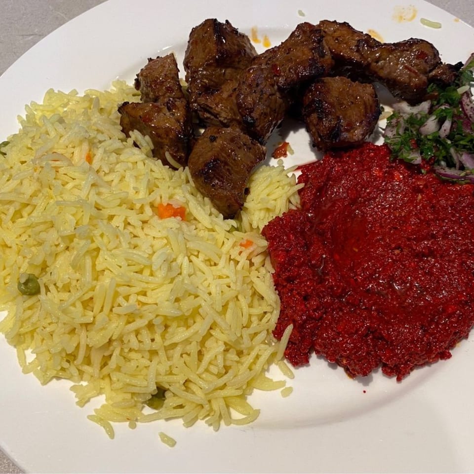 LE Chef Mediterranean plate with yellow rice, grilled meat, red sauce, and a side salad.
