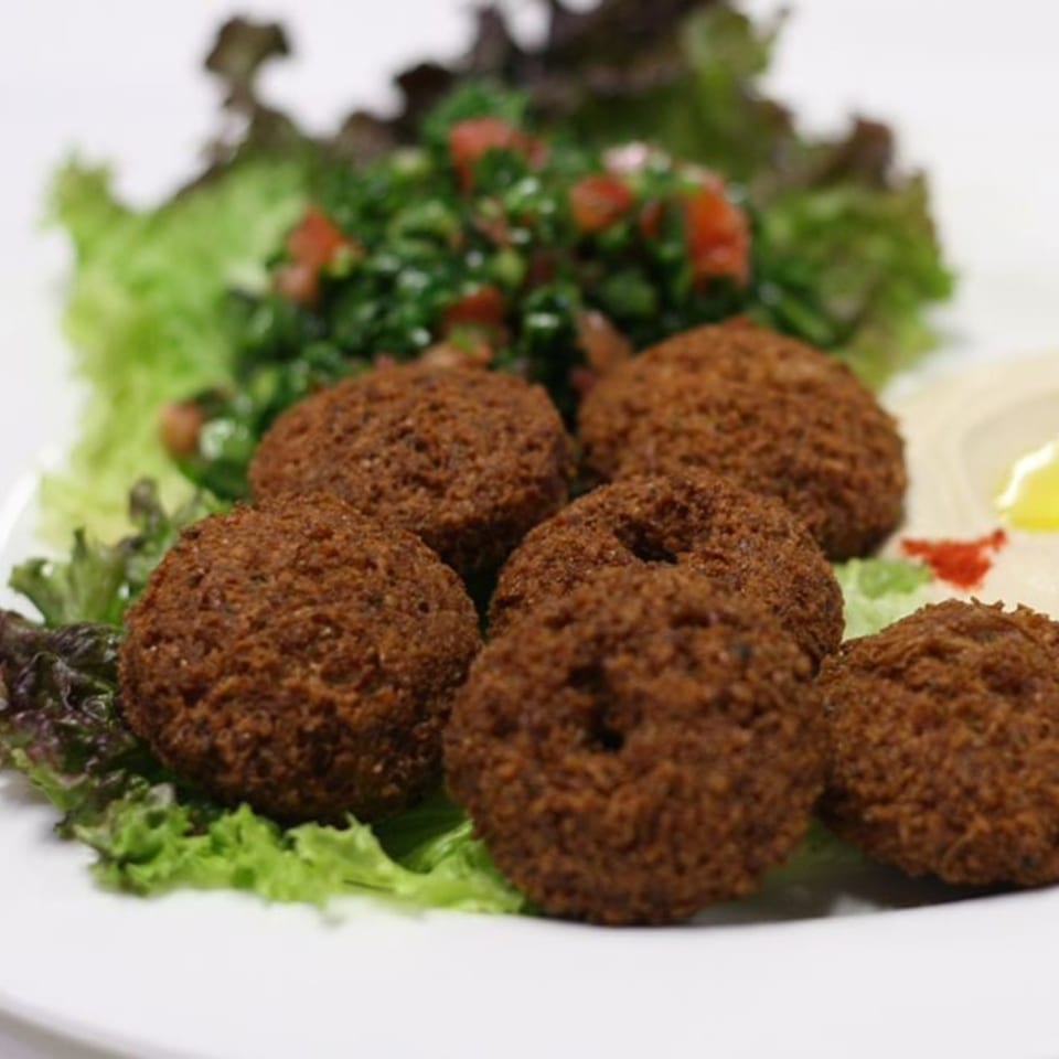 Crispy falafel balls with fresh tabbouleh salad and hummus on a white plate.