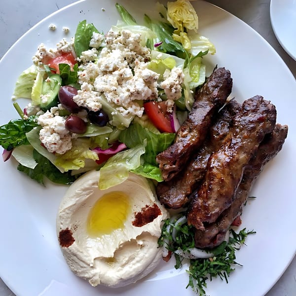LE Chef Mediterranean's plate with grilled meat, hummus, and a fresh salad topped with feta cheese.