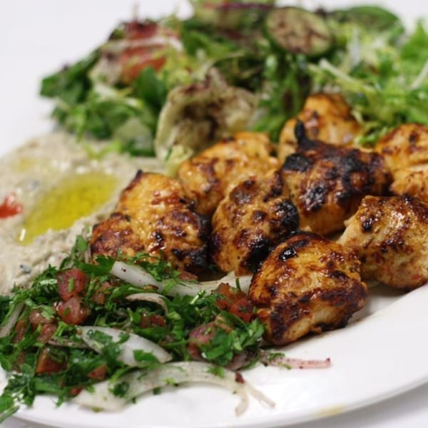 Grilled chicken pieces with fresh green salad, baba ghanoush, and tabbouleh on a white plate.