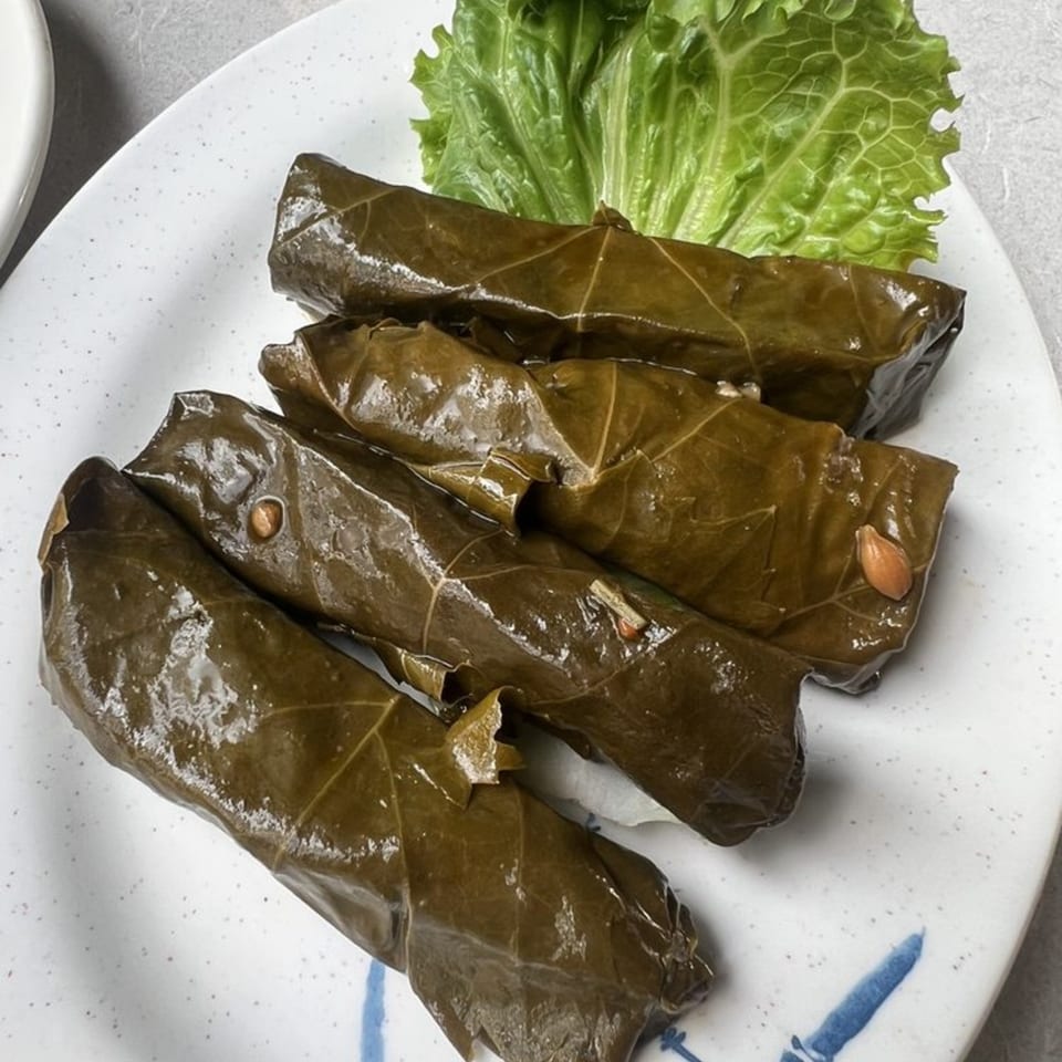 Four dolmades, or stuffed grape leaves, with a side of fresh green lettuce on a white plate.