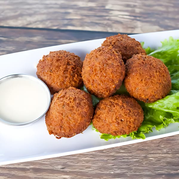Six crispy, golden-brown falafel balls on a bed of lettuce with a side of white dipping sauce.