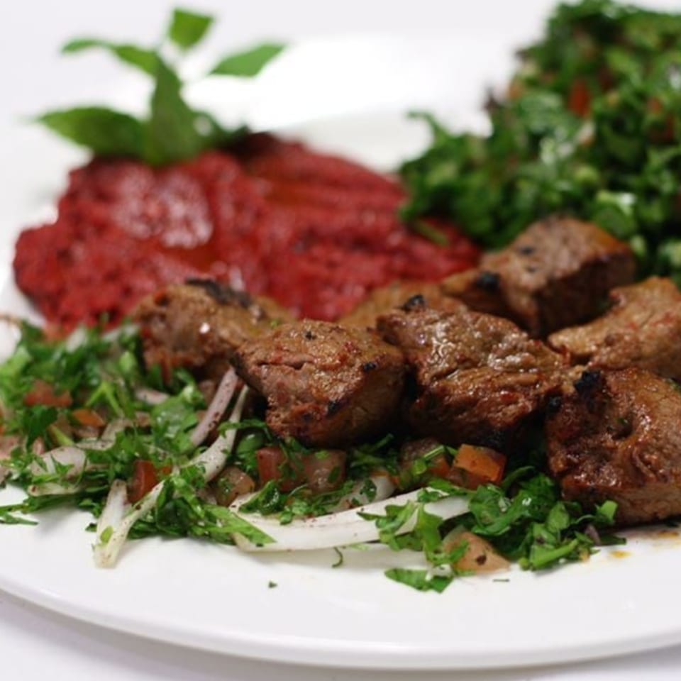 Grilled meat cubes with a side of red dip and green salad, garnished with mint.