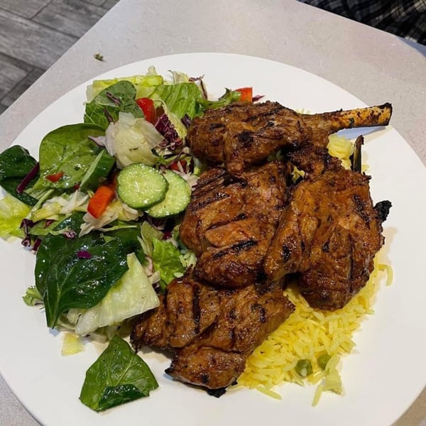 Grilled Mediterranean lamb chops with yellow rice and a fresh green salad on a white plate.