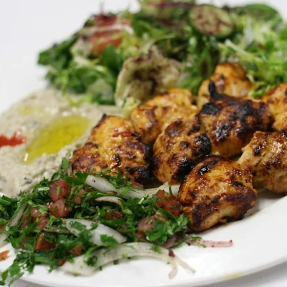 Grilled chicken pieces, baba ghanoush, and two fresh salads on a white plate at LE Chef Mediterranean.