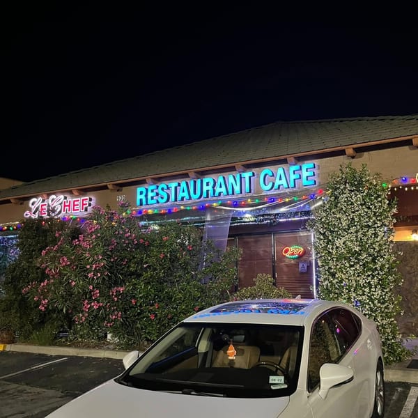 LE Chef Mediterranean Restaurant Cafe exterior at night, with neon signs and a white car in the foreground.