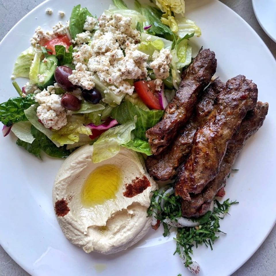 LE Chef Mediterranean plate with grilled meat skewers, hummus, and a fresh salad with feta.
