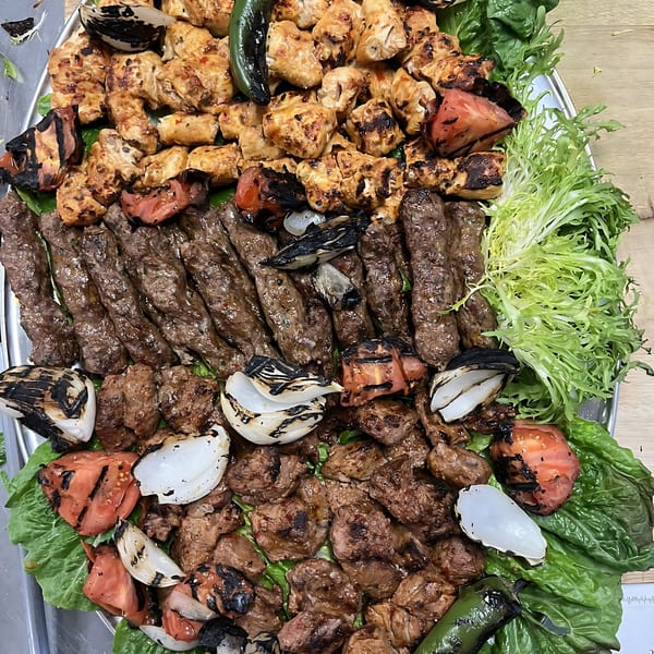 A large platter of grilled Mediterranean meats, including chicken, kofta, and beef, with charred vegetables and lettuce.