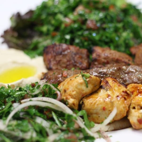 Grilled chicken and beef kebabs with hummus, tabbouleh, and a side salad with onions.