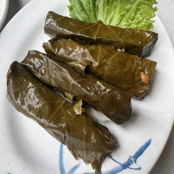 Four stuffed grape leaves (dolmades) with a side of lettuce on a white plate with blue accents.