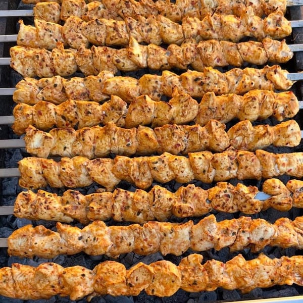 Rows of golden-brown chicken shish tawook skewers grilling over hot coals.